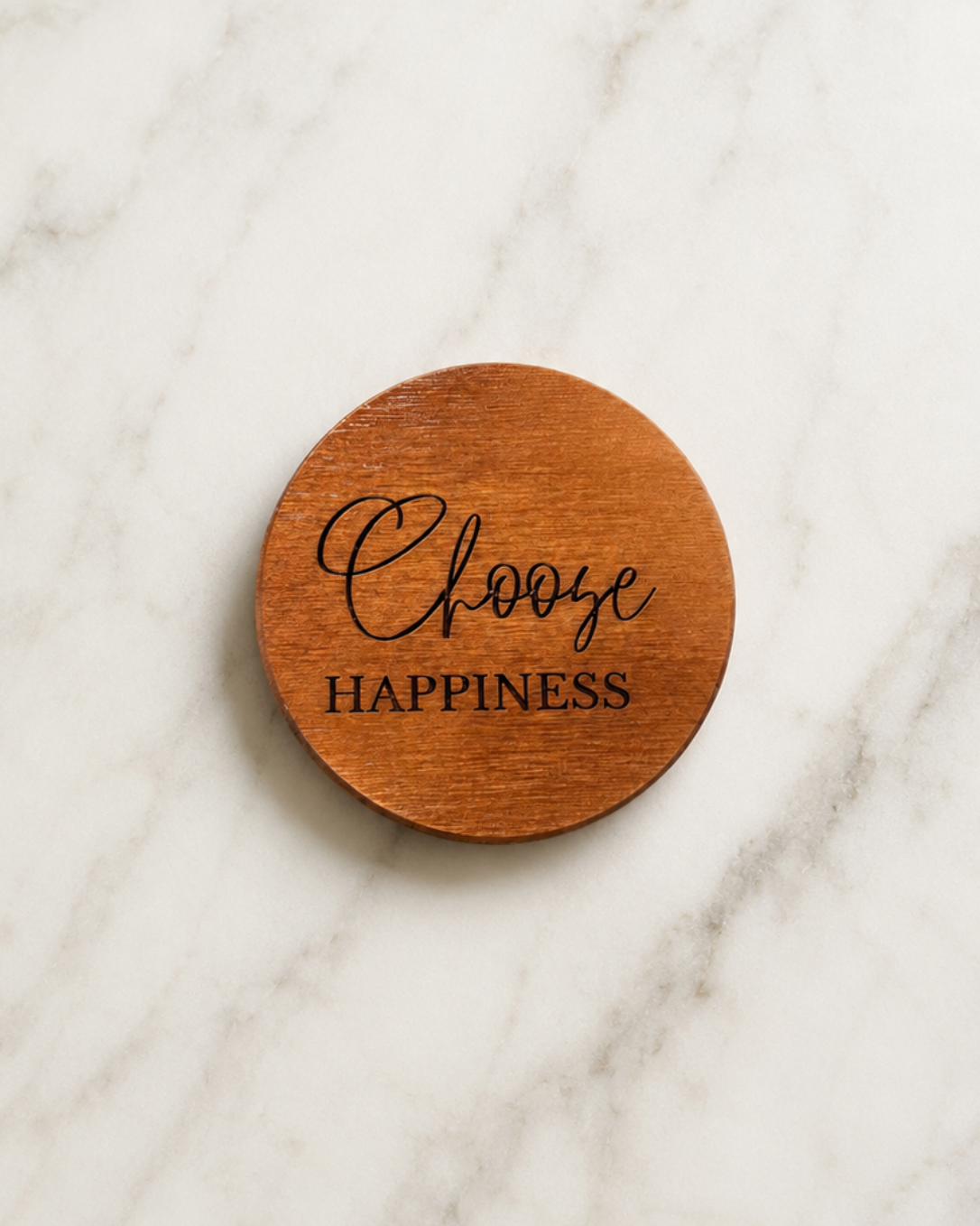 Wooden coaster with 'Choose Happiness' text laying on a marble surface